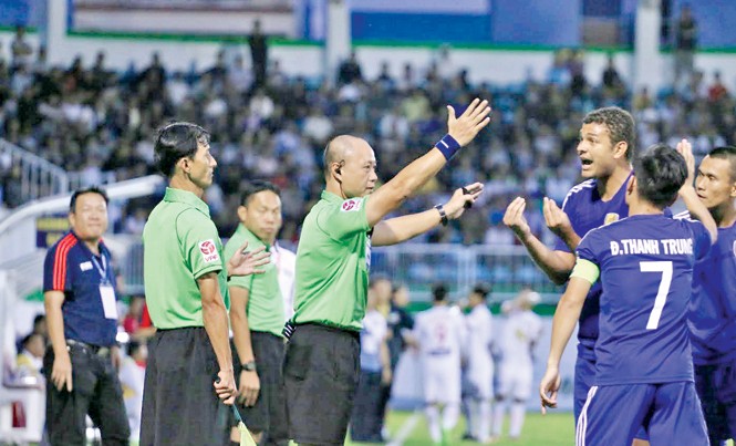Cuộc sống của những “ông vua sân cỏ” Trợ lý Phan Việt Thái (trái) và trọng tài Hoàng Anh Tuấn (giữa) bị cầu thủ Quảng Nam bao vây phản đối ở trận HAGL – Quảng Nam. Ảnh: Trần Khánh.