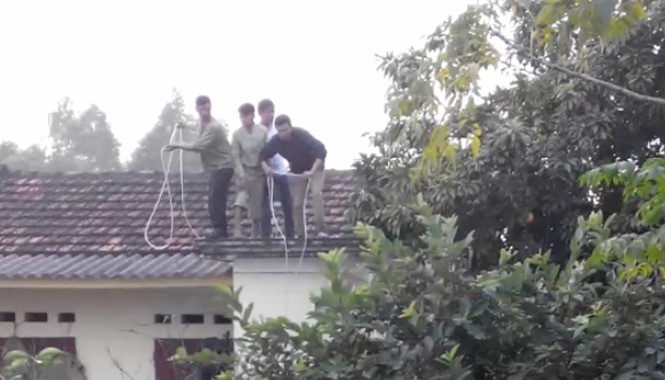Trâu chuẩn bị giết thịt nổi điên, húc người gãy chân Người dân phải đứng trên nóc nhà, quăng dây xuống nhằm giăng bẫy bắt "trâu điên". Ảnh cắt từ clip do nhân chứng cung cấp.