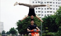 Nghệ sĩ Quốc Cơ - Quốc Nghiệp thực hiện động tác chồng đầu lên nhau khi đi xe máy có sự hỗ trợ của đoàn làm phim. Ảnh cắt từ clip gốc
