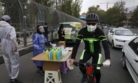 Một người đeo khẩu trang đi xe đạp qua quầy bán nước rửa tay ở Tehran ngày 16/4. (Ảnh: AP)