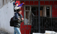 Một người đàn ông cùng con trai đi gần ngôi nhà bị hư hỏng ở Mariupol ngày 20/3. (Ảnh: Reuters) 