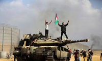 Người Palestine vẫy quốc kỳ của họ và ăn mừng bên một chiếc xe tăng Israel bị tịch thu trên Dải Gaza ngày 7/10. (Ảnh: AP)