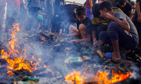 Người Palestine tìm lại đồ ăn trong đám cháy sau cuộc không kích của Israel vào khu lều của người di tản. (Ảnh: Reuters)
