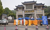 Người đàn ông đeo khẩu trang, mặc áo mưa xanh ôm ảnh người thân bên ngoài nghĩa trang Biandanshan ở Vũ Hán hôm 31/3. Ảnh: Getty.