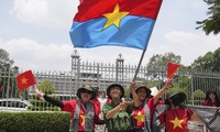 Người dân vẫy cờ Mặt trận Dân tộc Giải phóng miền Nam khi chụp ảnh trước Dinh Độc Lập ngày 29/4. (Ảnh: AP)