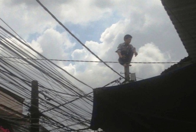 Thanh niên 'ngáo đá' đu dây điện như người nhện Nam thanh niên ngồi chồm hổm trên ngọn trụ điện.