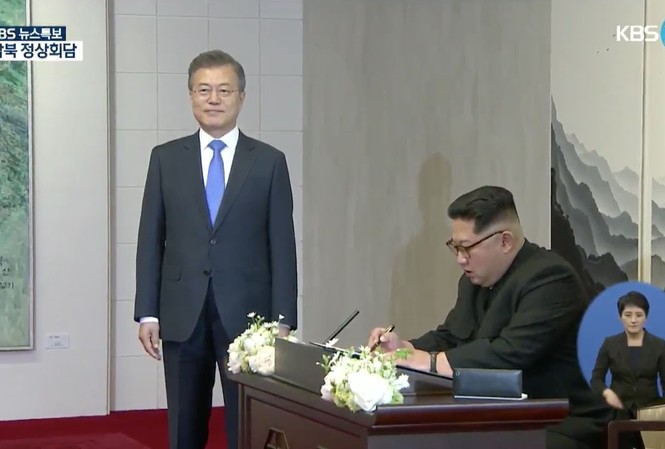 Nhân viên an ninh Triều Tiên phun thuốc khử trùng nơi ông Kim Jong-un ngồi Ông Kim Jong-un ngồi viết lưu bút sáng 27/4 tại Nhà Hòa Bình. Ảnh: KBS