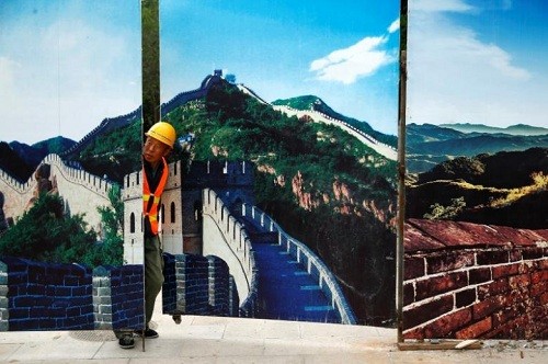 Trung Quốc xây nhà ga sâu, rộng nhất thế giới dưới Vạn Lý Trường Thành Một công nhân thò đầu khỏi hàng rào trang trí bằng tranh in đoạn Vạn Lý Trường Thành Bát Đạt Lĩnh, Bắc Kinh, hôm 1/9. Ảnh: Reuters.