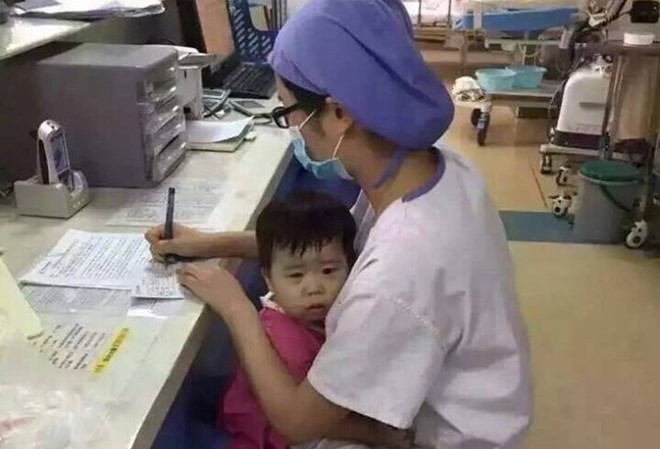 Xúc động trước nữ y tá vừa ôm bé gái mồ côi vừa làm việc Hình ảnh nữ y tá ôm bé gái mồ côi khi làm việc. (Nguồn: CCTV News)