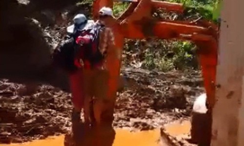 Giáo viên bám gàu máy xúc đến trường trước ngày khai giảng Thầy cô giáo đu gàu máy xúc qua điểm sạt lở (Ảnh cắt từ clip)