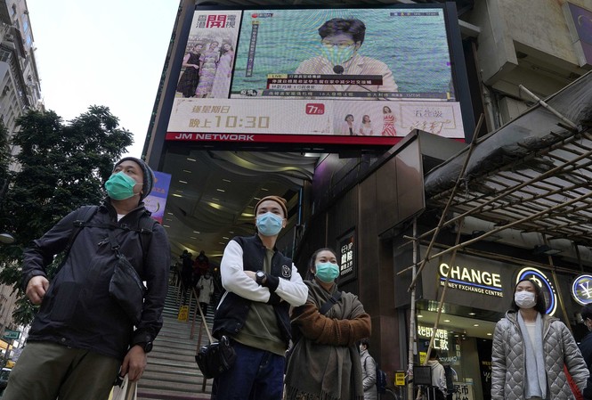 Hong Kong cân nhắc bắt người nghi nhiễm virus corona đeo vòng theo dõi Người dân Hong Kong đeo khẩu trang đứng trước màn hình TV chiếu hình ảnh bà Carrie Lam. Ảnh: AP.