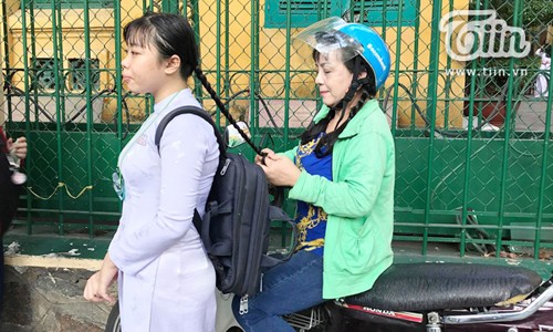 Hình ảnh ấn tượng mẹ tết tóc cho con gái trước lễ bế giảng Người mẹ ngồi trên xe máy thắt bím cho con gái trước cổng trường.