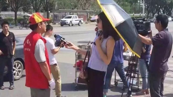 Nữ phóng viên bị đình chỉ vì đeo kính, che ô lúc tác nghiệp Bức hình nữ phóng viên đeo kính râm, che ô trong lúc tác nghiệm gây tranh cãi.