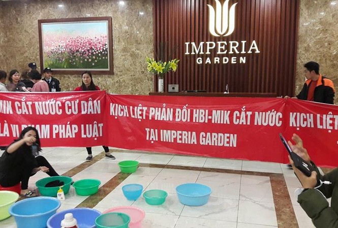 Bị cắt nước đầu năm, cư dân chung cư 203 Nguyễn Huy Tưởng mang băng rôn và xô chậu xuống sảnh phản đối.