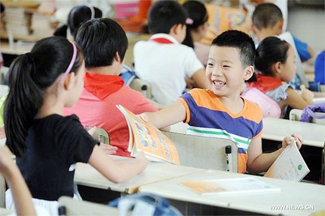 Bé trai học sinh tiểu học trường thực nghiệm Baochuta ở Hàng Châu, Chiết Giang, Trung Quốc quay xuống bàn dưới đưa sách cho bạn với nụ cười rạng rỡ trong ngày khai giảng 1/9