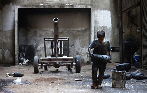 Cậu bé Issa (10 tuổi) đang bê quả bom tại một nhà máy sản xuất vũ khí của Quân đội tự do Syria tại Aleppo ngày 7/9. Cuộc khủng hoảng ở Syria kéo dài hơn 3 năm đã biến nhiều cậu bé thành những tay súng hoặc thợ sửa vũ khí.