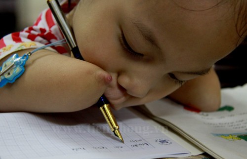 Để viết được chữ, Chi kẹp chiếc bút máy được vào một bên tay và miệng. Mỗi nét chữ đưa đi, tay và miệng Chi lại di chuyển theo. Ảnh: Trường Phong