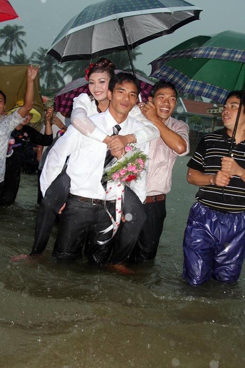 Cơn mưa nặng hạt trên đầu trong khi nước dâng ngập đến gối vẫn không làm sờn lòng chú rể Hưng, một lính hải quân tại Cam Ranh, Khánh Hòa, bên cạnh cô dâu của mình. Ảnh: HN Live