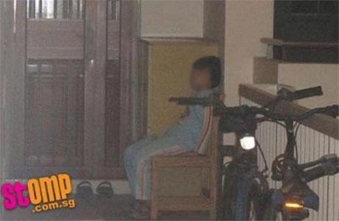 Một bé trai trong bộ đồ ngủ đã bị người thân đuổi ra khỏi nhà, bắt phải ngủ trên chiếc ghế nhỏ, co ro trong thời tiết lạnh khi đồng hồ điểm 10 giờ tối