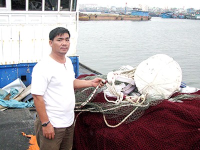 Ngư dân Trương Văn Hai với con tàu từng trầy trật vì bảo hiểm Ảnh: Nam Cường