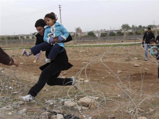 Người Syria nhảy qua hàng rào dây thép gai khi chạy trốn khỏi thị trấn Ras al-Ain sang thị trấn Ceylanpinar, tỉnh Sanliurfa, Thổ Nhĩ Kỳ.