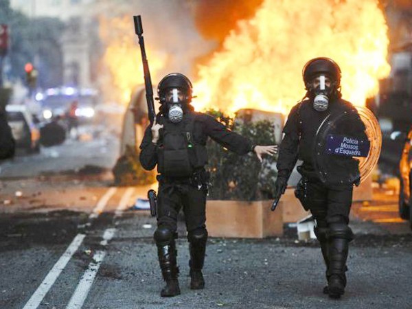 Cảnh sát chống bạo động đi ngang các thùng rác bị người biểu tình đốt ở thành phố Barcelona ngày 29-3 Ảnh: Getty Images