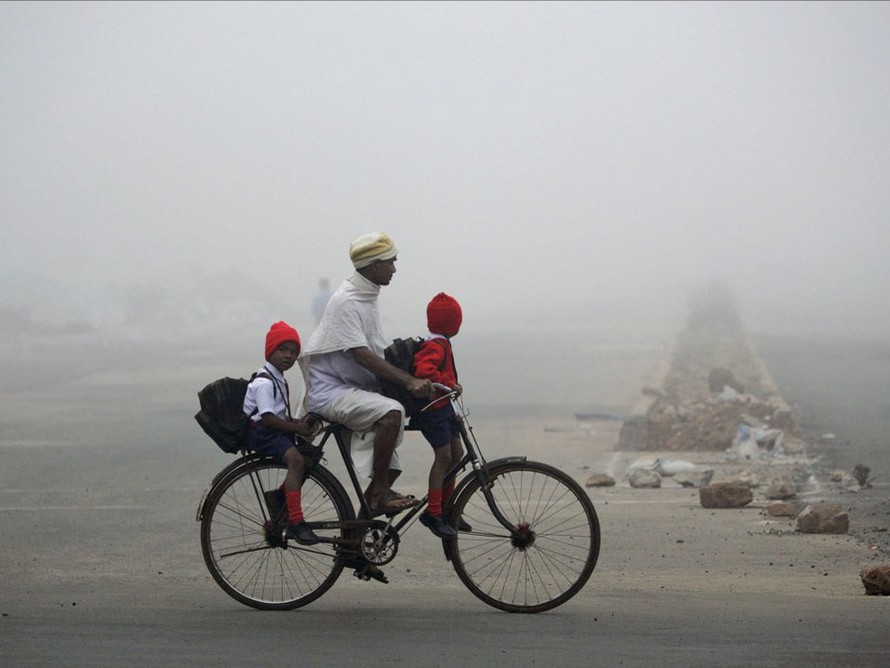 Một người đàn ông chở 2 con đi học bằng xe đạp giữa trời đầy sương mù ở Bhubaneswar, Ấn Độ