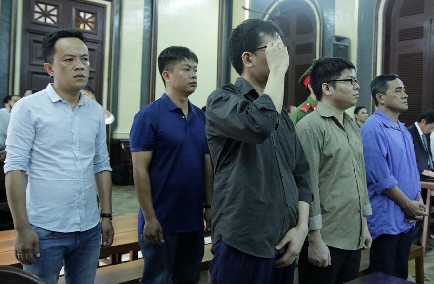 Cựu công an Bùi Khắc Hà (đứng, tay che mặt) và Nguyễn Giang Lam (đứng, áo vàng), cùng 3 bị cáo. Ảnh: Tân Châu