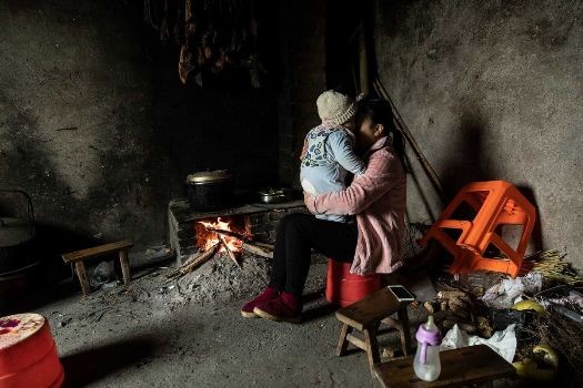 Chị Xie Xianmei ôm con trai khi đang ngồi đun bếp trong gia đình bố mẹ nuôi ở Dazhou. (Ảnh: Bloomberg)