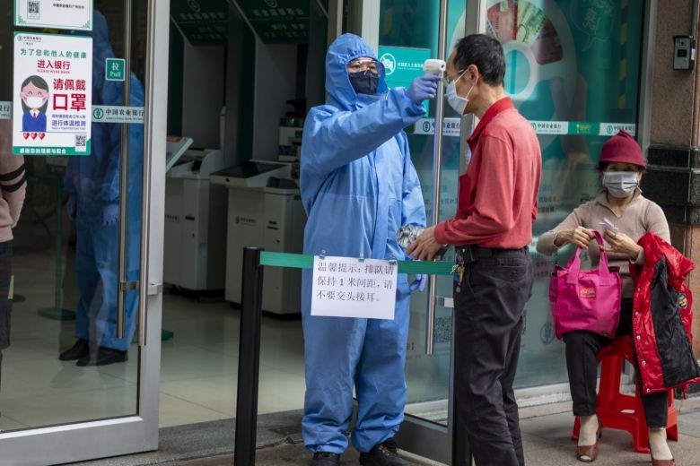 Một nhân viên bảo vệ kiểm tra thân nhiệt của khách hàng vào chi nhánh ngân hàng ở Quảng Châu. (Ảnh: EPA-EFE)