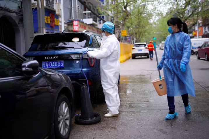 Một phụ nữ mặc đồ bảo hộ y tế trong khi rửa xe ô-tô trên đường phố ở Vũ Hán. (Ảnh: Reuters)