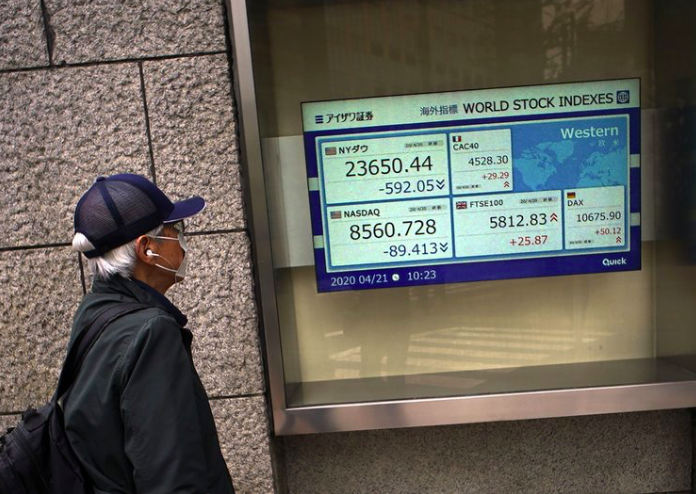 Một người đàn ông đeo khẩu trang nhìn bảng điện tử chỉ số chứng khoán thế giới bên ngoài một công ty chứng khoán ở Tokyo ngày 21/4. (Ảnh: AP)
