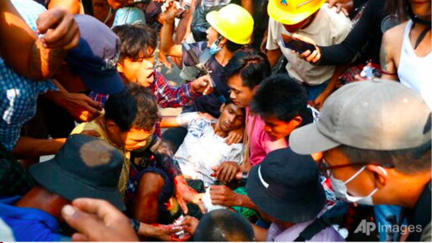 Đám đông vây quanh một người biểu tình bị thương ở Hlaing Tharyar ngày 14/3. (Ảnh: AP)