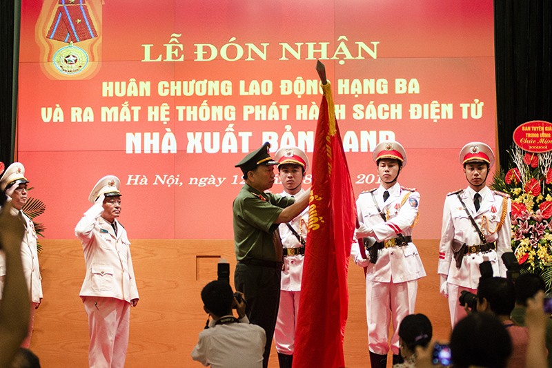 Bộ trưởng Công an Tô Lâm gắn Huân chương Lao động hạng Ba lên lá cờ truyền thống của NXB CAND.