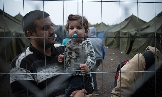 Một người Syria bế con trong khu trại ở khu vực biên giới Hungary – Serbia, nơi họ phải lấy dấu vân tay để đăng ký tị nạn