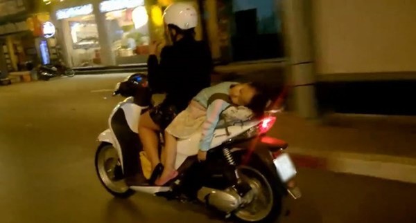 Em bé không được đội mũ bảo hiểm, nằm ngủ gật trên xe của mẹ.