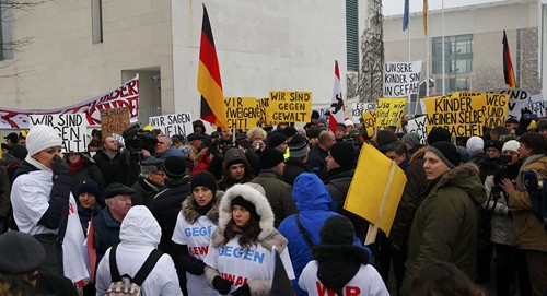 Người biểu tình mang theo các biểu ngữ phản đối, tập trung bên ngoài dinh Thủ tướng Đức Angela Merkel sau khi câu chuyện của bé gái lan truyền. Ảnh: Reuters
