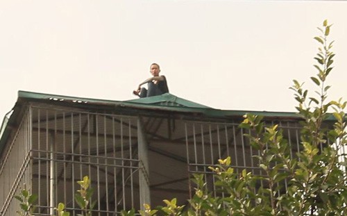 Nam thanh niên cố thủ trên mái tôn tầng 4 suốt nhiều giờ. Ảnh: Mai Anh.