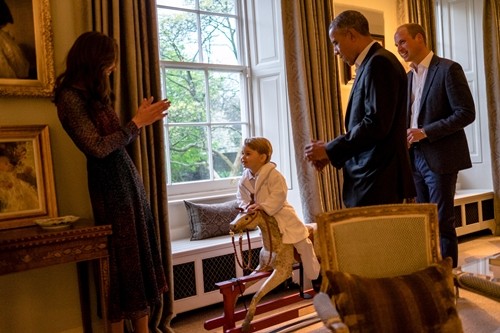 Hoàng tử bé George chơi ngựa gỗ cùng với Công nương Catherine, đứng cạnh là Tổng thống Mỹ Barack Obama (thứ 2 từ phải sang) và Hoàng tử William, tại Cung điện Kensington ngày 22/4. Ảnh: PA/Reuters.