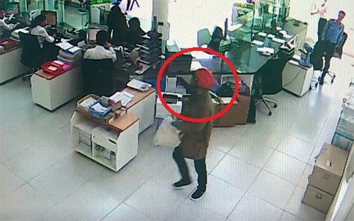 Tên cướp (khoanh tròn đỏ) cầm bao tải trắng tiến thẳng vào quầy gom tiền. Ảnh: Cắt từ video