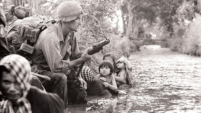 Hai em bé Việt Nam nhìn chằm chằm vào một lính dù Mỹ cầm khẩu súng phóng lựu M79 (ảnh chụp trong ngày đầu tiên của năm 1966, tại một con mương cách Sài Gòn 20km). Ảnh: Horst Fass