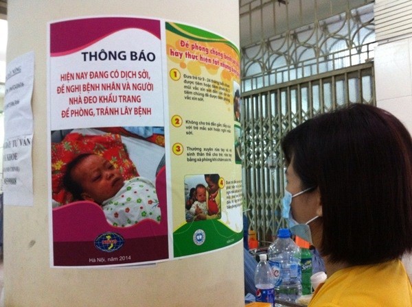  Người dân đọc khuyến cáo về phòng bệnh sởi. Ảnh: Thùy Giang/Vietnam+)