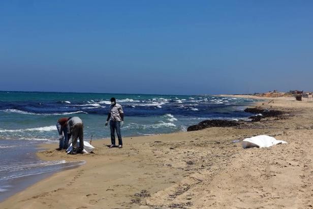 Những người đàn ông tìm thấy thi thể của một nạn nhân xấu số bị dạt vào bờ biển Libye, cách Tripoli 60km về phía Đông. Ảnh: AFP