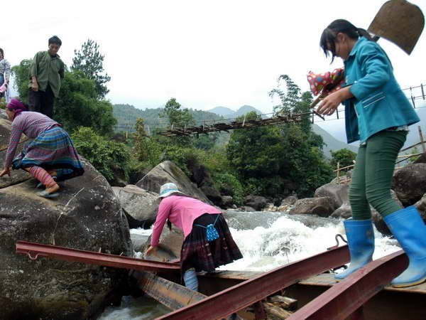 Người dân vượt suối bằng những thanh sắt của cầu tạm bị lũ cuốn trôi rất nguy hiểm. (Ảnh: Nguyễn Công Hải/TTXVN)