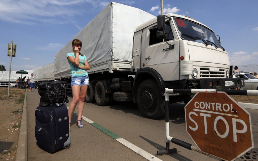 Đoàn xe tải mang hàng cứu trợ nhân đạo tới Ukraine qua khu vực Donetsk trên biên giới Nga-Ukraine, khi một phụ nữ đợi con trai trốn khỏi vùng chiến sự phía Đông Ukraine và có thể đã vượt biên sang vùng Rostov của Nga, hôm 22/8/2014. ( REUTERS/Alexander De