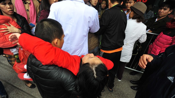 Một phụ nữ bị ngất xỉu khi xếp hàng chờ để tiêm vắc-xin dịch vụ cho con từ rạng sáng ngày 25/12/2015 tại số 182 Lương Thế Vinh, Hà Nội. Ảnh: Giang Huy.