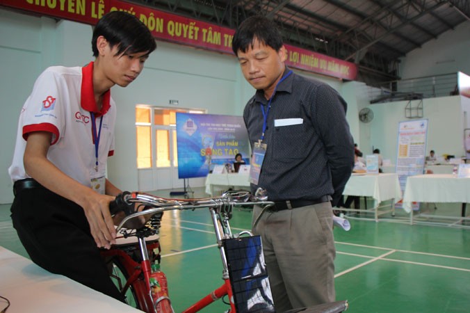 Mai Quốc Huy (bên trái) hướng dẫn sử dụng chiếc “xe đạp thông minh” của mình. Ảnh: NGÔ TÙNG.