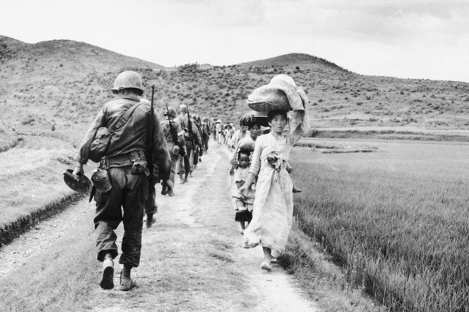 Lính Mỹ hành quân trong khi đoàn người tị nạn di chuyển theo chiều ngược lại, tại khu vực sông Nakdong, trong chiến tranh Triều Tiên.