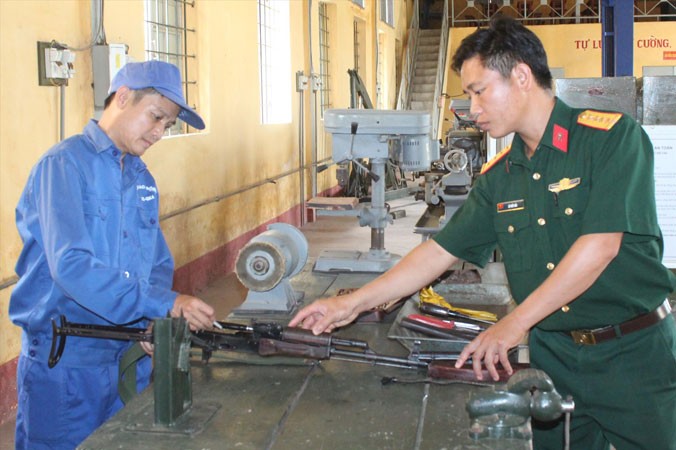 Thiếu tá Quang (bên trái) đang sửa chữa súng tiểu liên AK tại đơn vị.