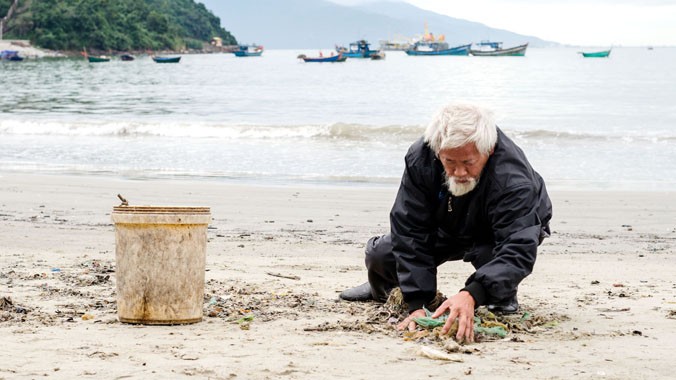 Cụ Mạo đang nhặt rác trên bãi biển Nam Ô. Ảnh: Tấn Lực